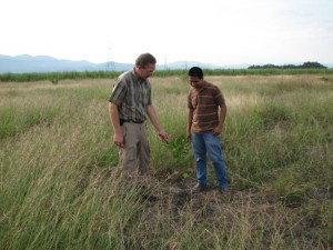Cleo Yoder and Luis Flores examining fruit tree sappling on land site. This is approximately where one of the buildings will sit.