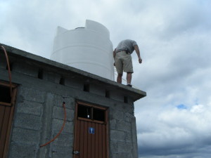 Placing the water storage tank onto the roof of the outhouse. The water is fed into the house with gravity pressure